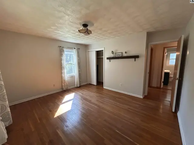 Spacious bedroom with hardwood floors, a closet, and a view into an en-suite bathroom.
