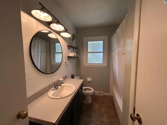 Modern bathroom with a white vanity, round mirror, shiplap accent wall, and a tub/shower combo.