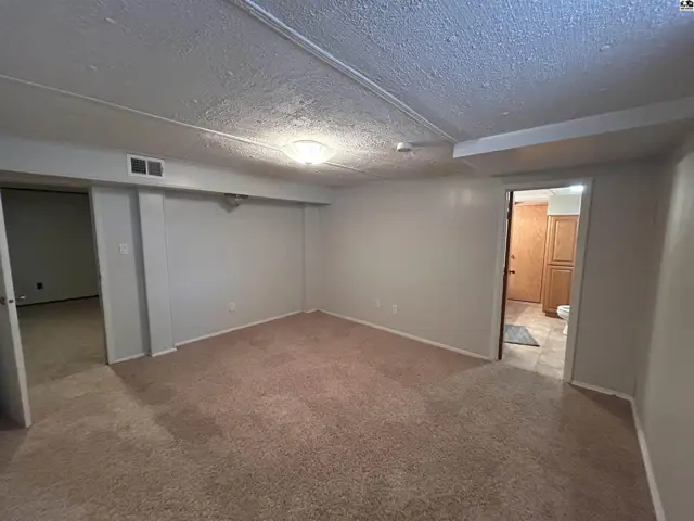 Spacious room with plush carpet, neutral walls, and a doorway leading to a hallway.