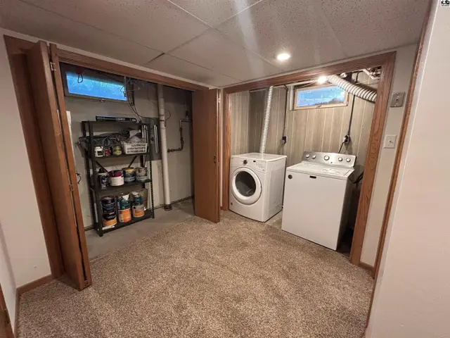 Laundry room with white washer and dryer, carpet, and storage shelves.
