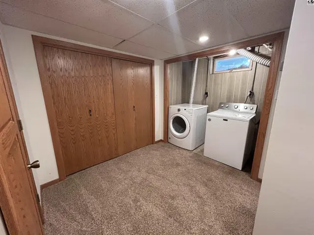 Basement laundry area with wood-paneled walls, white washer and dryer, and large wood-paneled closet doors.