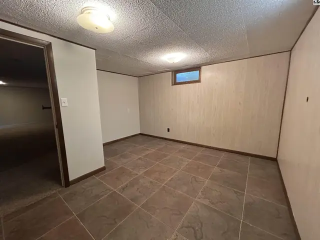 Finished basement room with textured walls, large tile flooring, and a small window.