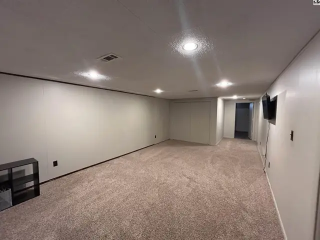 Spacious finished basement with plush carpet, recessed lighting, and a wall-mounted TV.