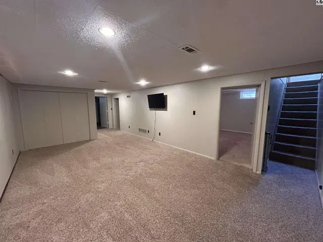 Spacious finished basement with plush carpet, recessed lighting, and a mounted television.