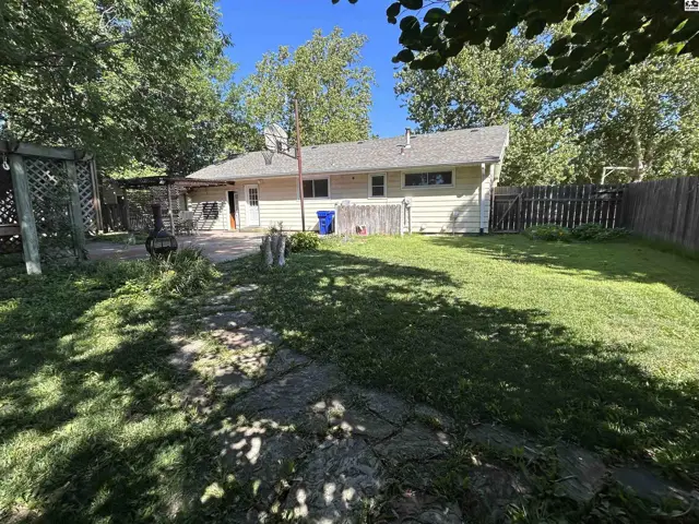 Backyard with a stone path, patio, and wooden fence surrounding a light yellow house.