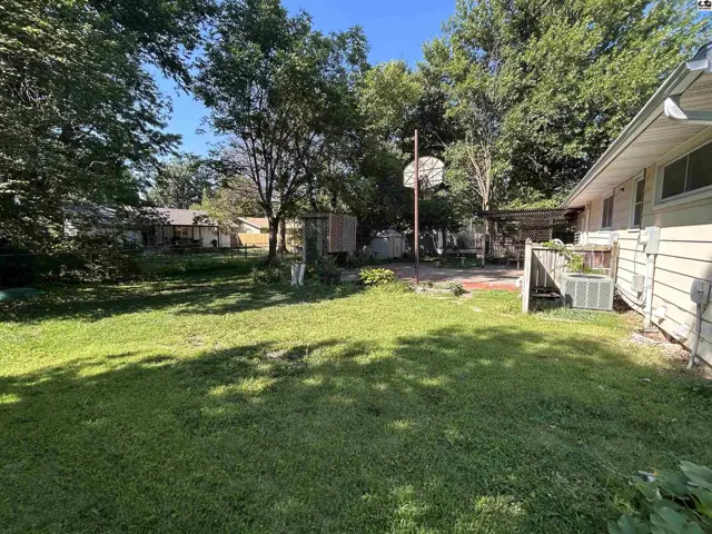 Spacious backyard with a basketball hoop, patio, and mature trees.