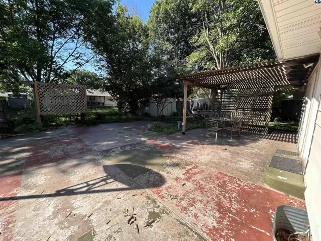 Spacious concrete patio with a wooden pergola, outdoor seating, and a fenced backyard.