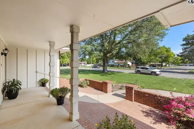 Covered porch with white columns and brick accents, leading to a manicured lawn and street view.