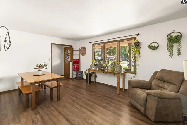 Living room with wood-look flooring, a recliner, dining set, and abundant natural light from a large window.