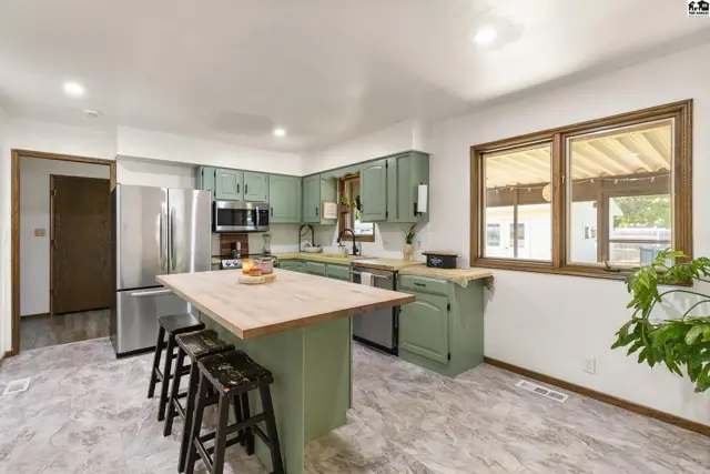 Spacious kitchen with sage green cabinets, stainless steel appliances, and a butcher block island with seating.