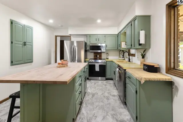 Spacious kitchen with sage green cabinets, butcher block island, stainless steel appliances, and light gray flooring.