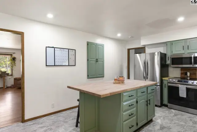 Spacious kitchen with sage green cabinets, butcher block island, stainless steel appliances, and light gray flooring.