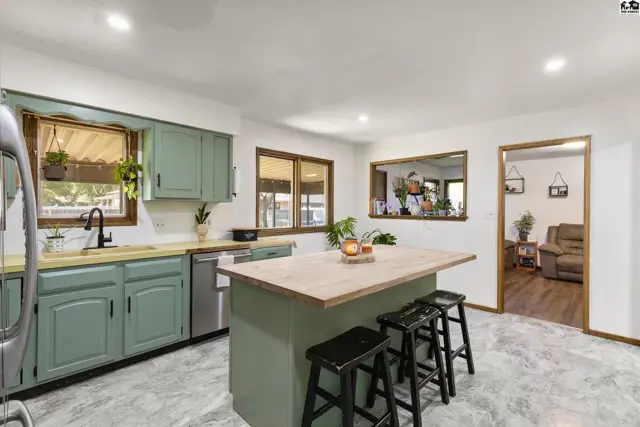 Spacious kitchen with sage green cabinets, a butcher block island, and marble-look flooring.