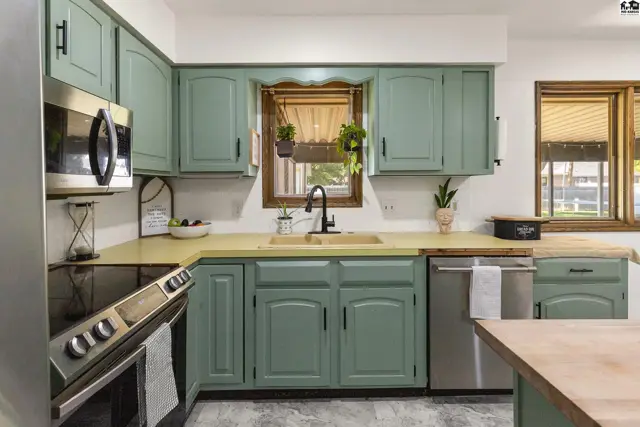 Kitchen with sage green cabinets, light wood countertops, stainless steel appliances, and a farmhouse sink.
