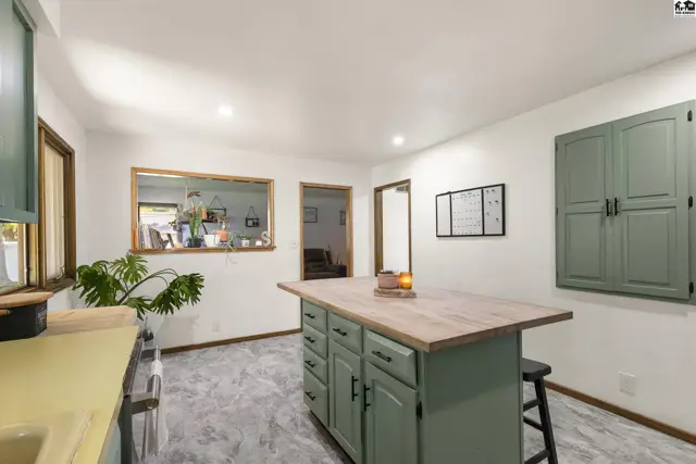 Kitchen with sage green island, butcher block countertop, and gray tile flooring.