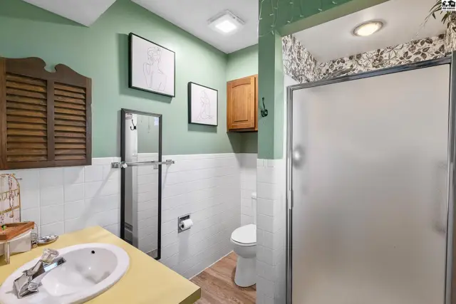 Bathroom with green walls, white tile, wood vanity, and frosted glass shower stall.