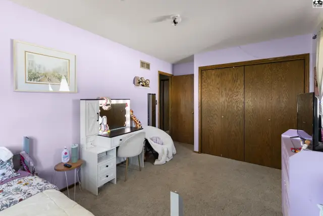 Lavender bedroom with a white vanity, mirrored closet doors, and carpeted floor.