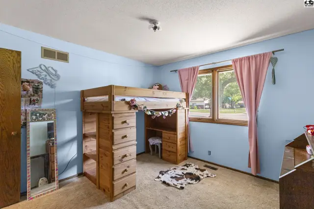 Light blue bedroom features a wooden loft bed with integrated desk and storage, pink curtains, and a cowhide rug.