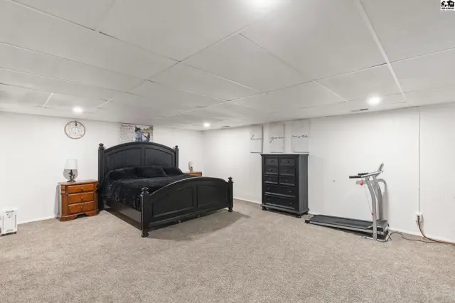 Spacious bedroom with a black bed frame, dresser, treadmill, and plush carpet.