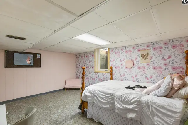 Bedroom with floral wallpaper, a wooden bed frame, and a mounted television.