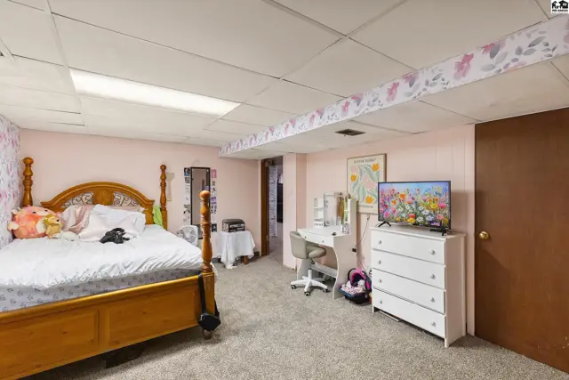 A bedroom with a wooden bed frame, white dresser, desk, and floral wallpaper accents.