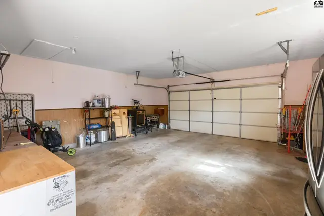 Spacious garage with concrete floor, light pink walls, wood wainscoting, and a large overhead door.