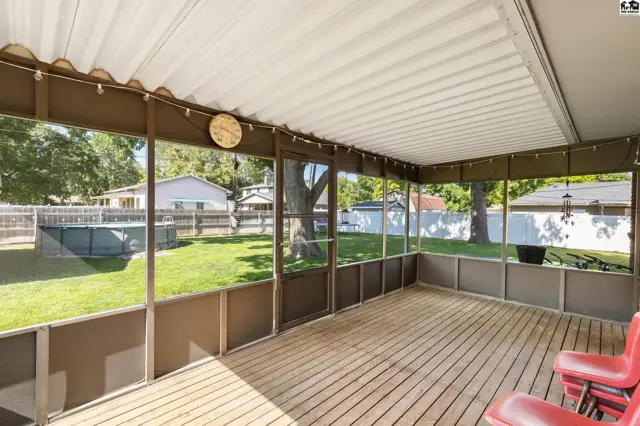 Screened-in porch with wood deck and ceiling fan overlooks a backyard with a pool.