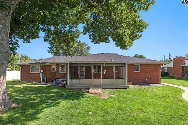 Brick ranch home with a screened-in porch and large backyard under a mature tree.