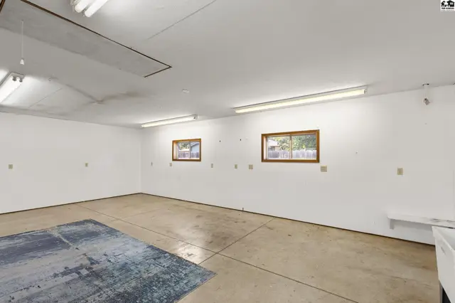 Spacious garage with concrete floor, white walls, fluorescent lighting, and two small windows.