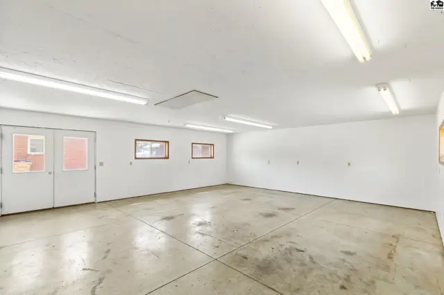 Spacious, unfinished interior with concrete floors, white walls, and fluorescent lighting.