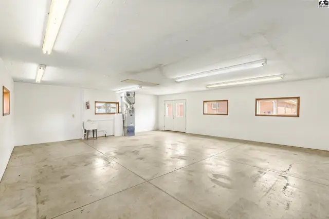 Spacious garage with concrete floors, white walls, multiple windows, and double doors.