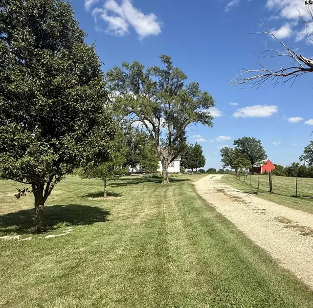 Gravel driveway leads to a white farmhouse surrounded by mature trees and a red barn.