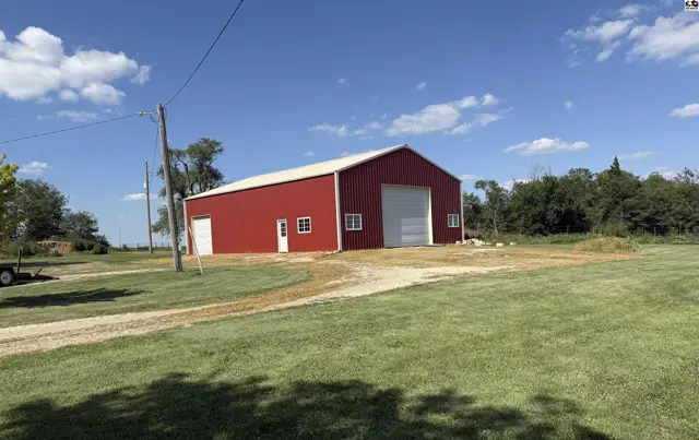 Red metal barn with white trim and large garage doors sits on a grassy lot.