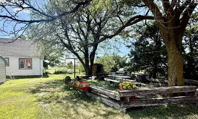 Spacious backyard with mature trees, picnic tables, and rustic wooden seating.