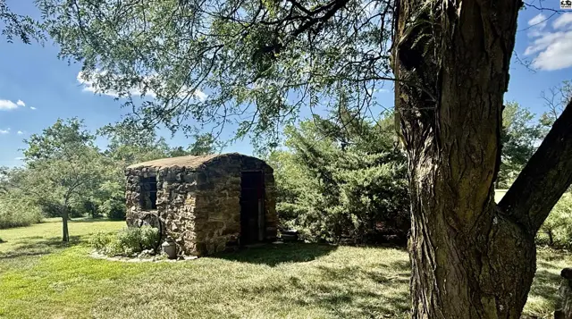 Rustic stone structure with a rounded roof sits in a grassy yard surrounded by trees.