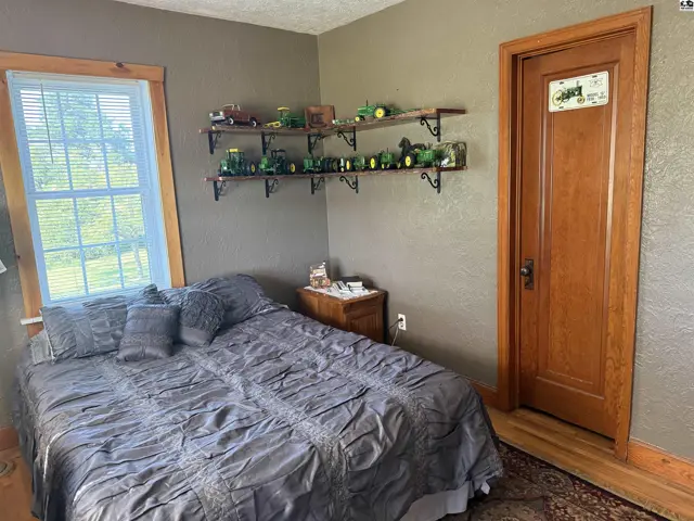 Bedroom with a queen-size bed, wooden door, and shelves displaying toy tractors.