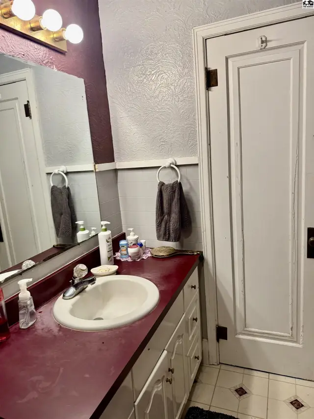 Bathroom vanity with a white sink, maroon countertop, and a large mirror reflecting a towel rack.