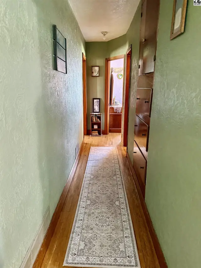 Hallway with light green textured walls, hardwood floors, and built-in wooden cabinets.