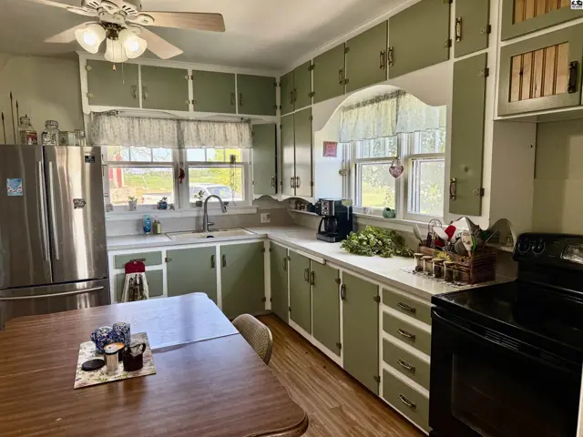 Kitchen with sage green cabinets, white countertops, stainless steel refrigerator, and a wooden dining table.