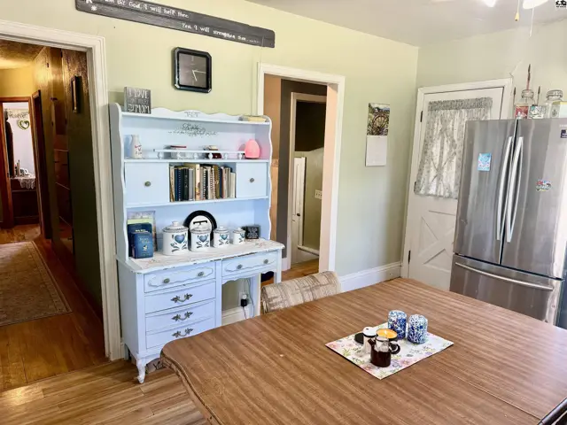 Light-filled kitchen with a blue hutch, stainless steel refrigerator, and wooden table.