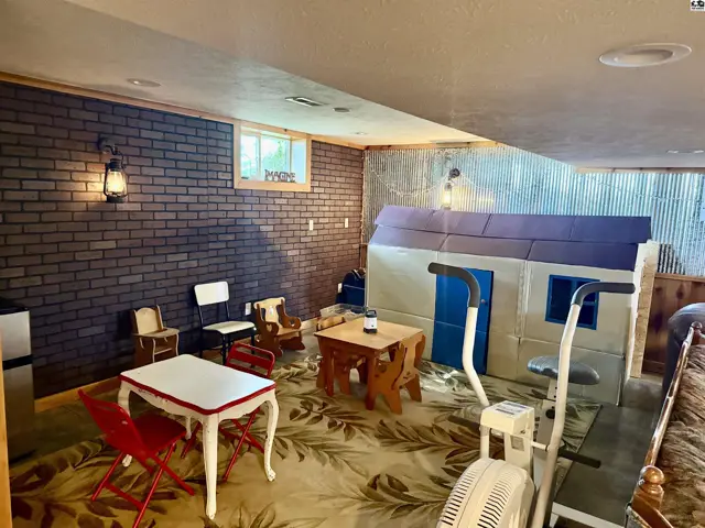 Cozy basement playroom features a faux brick wall, playhouse, exercise equipment, and colorful children's furniture.