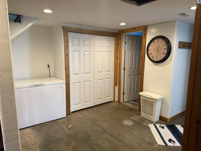 Basement room with concrete floor, white paneled doors, and a large chest freezer.