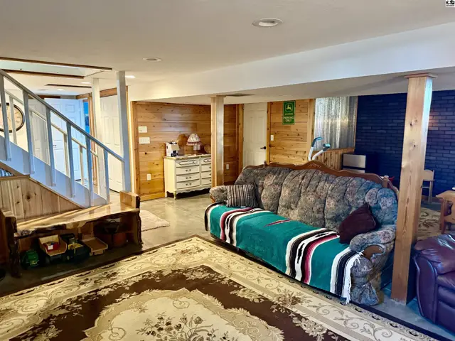 Cozy living room with wood paneling, a large patterned sofa, and a rustic staircase.