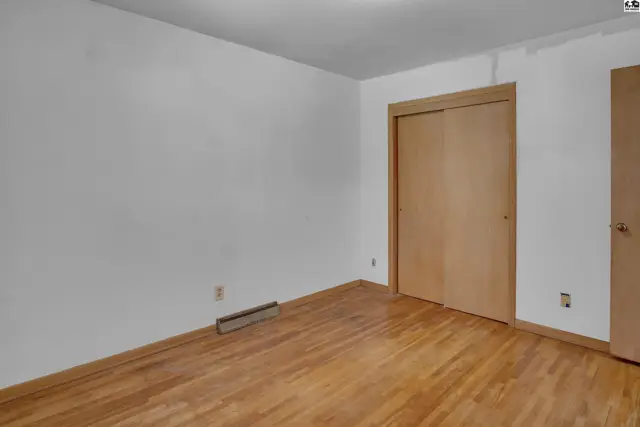 Empty bedroom with white walls, hardwood floors, and a light wood sliding closet door.