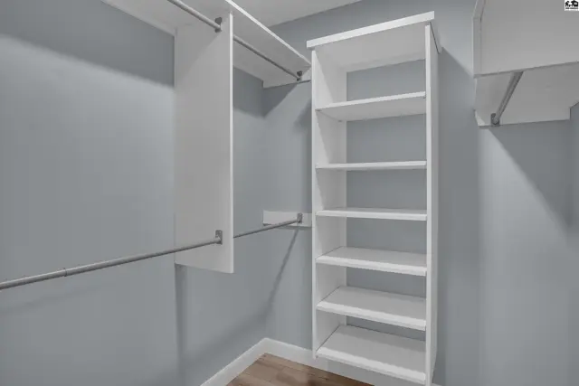 Spacious walk-in closet with white shelving, hanging rods, and light gray walls.