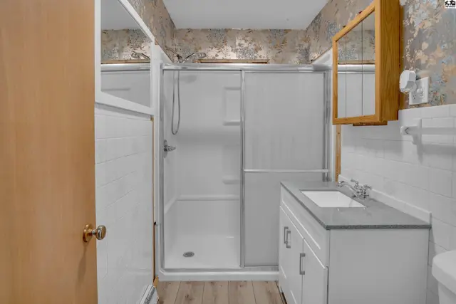 Modern bathroom with a walk-in shower, white vanity, and textured wallpaper.