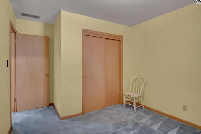 A bedroom with pale yellow walls, a carpeted floor, and two wooden closet doors, one with a white chair.