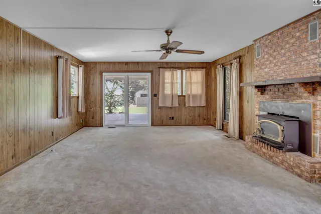Spacious living room with wood-paneled walls, a brick fireplace with wood stove, and sliding glass doors.
