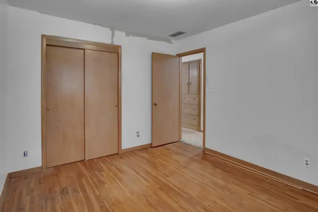 Spacious bedroom with hardwood floors, white walls, and a large closet with wood-paneled doors.