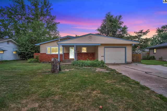 Single-story home with brick accents, a covered porch, and an attached garage under a colorful twilight sky.